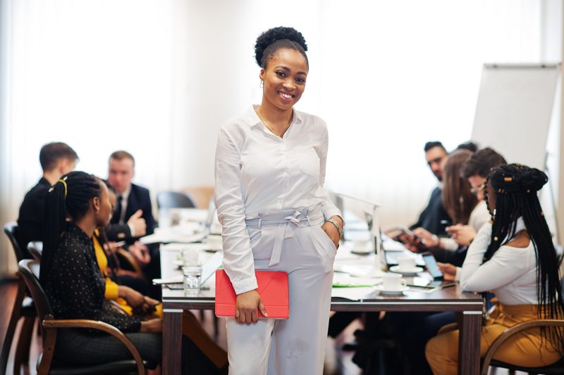 Face of handsome african american business woman, holding tablet on the background of business peoples multiracial team meeting, sitting in office table.